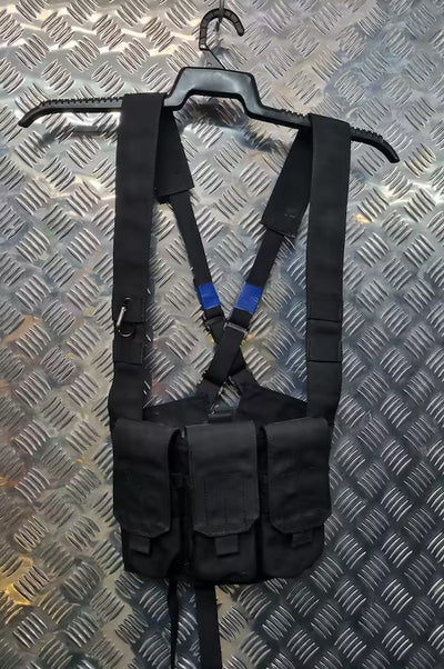 Black tactical vest with multiple pouches on a hanger against a metallic background