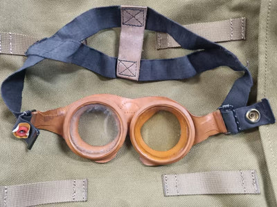 Vintage-style goggles with leather straps on a green fabric background