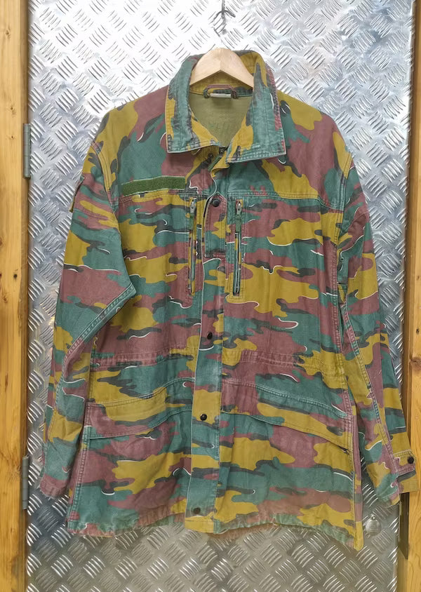 Camouflage jacket on a hanger against a metallic wall.