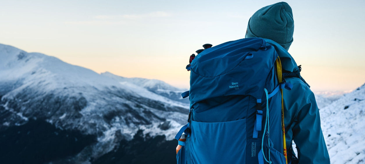Person with a blue backpack standing in the mountains at sunset.