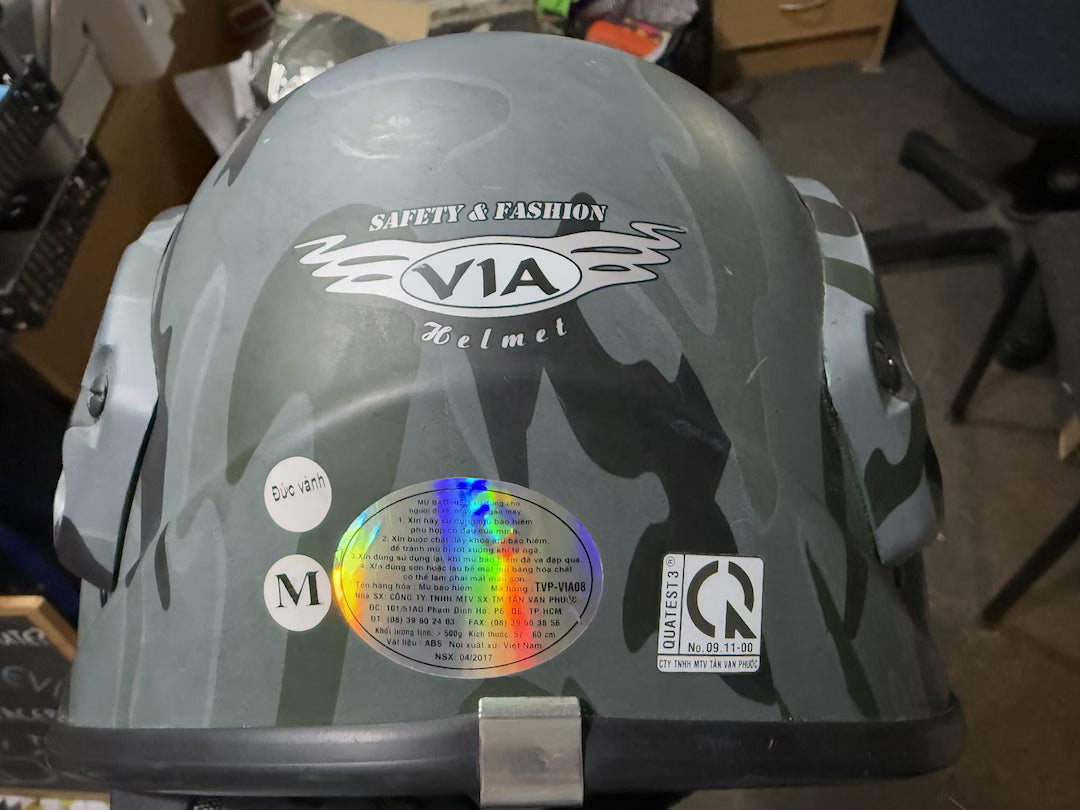 Gray helmet with 'VIA Helmet' branding and safety certification logos on a blurred indoor background.