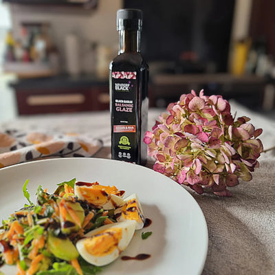 Balsamic Glaze bottle on a table with a salad and flowers