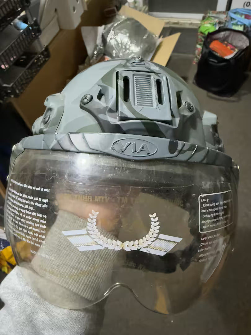 Helmet with clear visor held by a gloved hand, with a blurred background