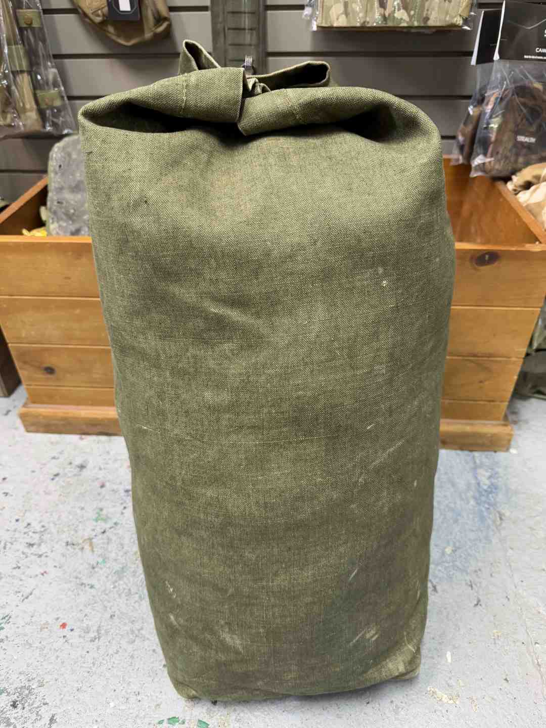 Green canvas bag on a concrete floor with wooden shelves in the background