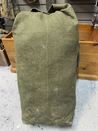 Green canvas bag on a concrete floor with wooden shelves in the background