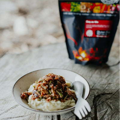 Bowl of food with a spoon on a wooden surface, with a package in the background.