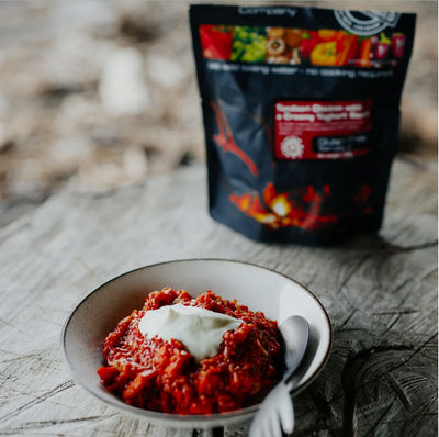 Bowl of red dish with a spoon on a wooden surface, with a package in the background.