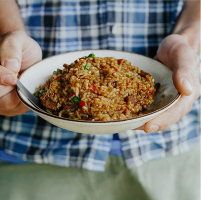 Person holding a bowl of fried rice with a blue plaid shirt in the background