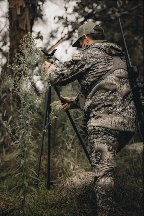 Hunter in camouflage gear using a bow in a forest setting