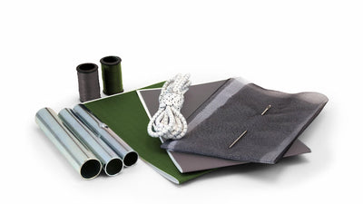 Collection of camping and outdoor gear including a green notebook, gray fabric pouch, and metal tubes on a white background.
