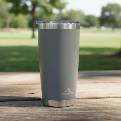 Gray insulated tumbler with a visible brand logo on a wooden surface with a park background.