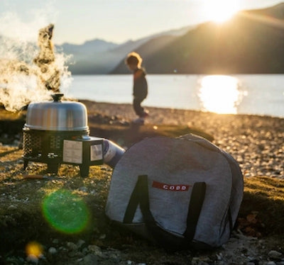 Person by a lake with a backpack and portable stove at sunset
