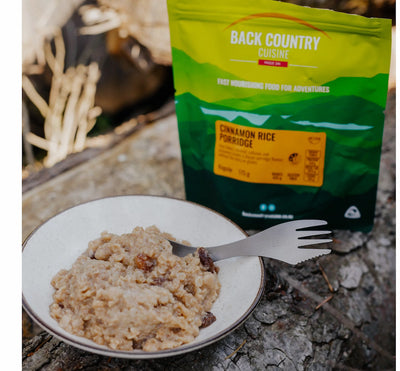 Back Country Cuisine cinnamon rice porridge package with a bowl of porridge and a fork on a stone surface.