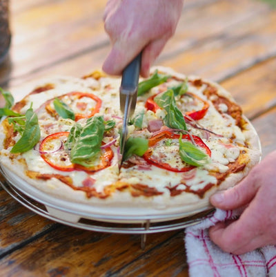 Person cutting a pizza with a fork and knife on a wooden table