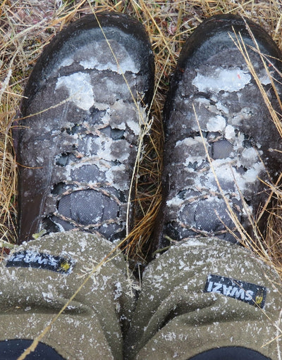 Pair of worn boots with visible wear and snow on a grassy background