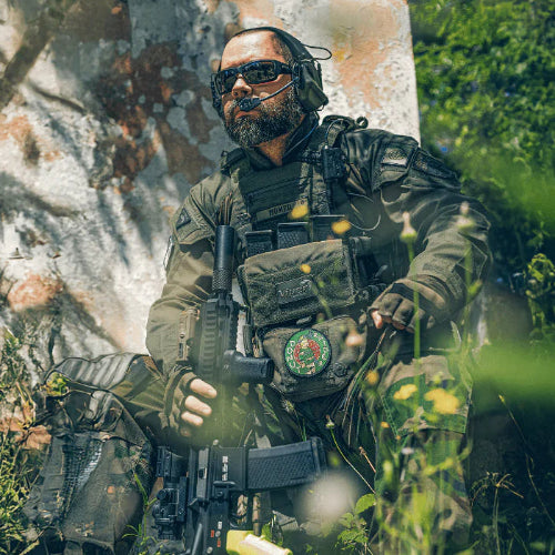 Person in tactical gear holding a rifle in a forest setting