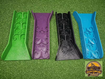 Four decorative plastic shims in green, purple, black, and blue on a green textured surface with a brand logo in the corner.