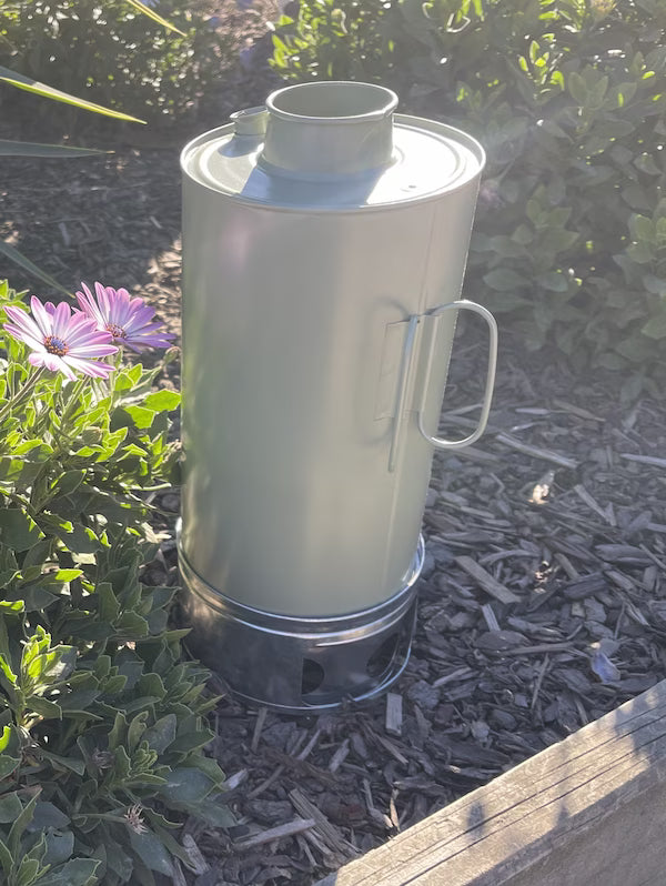 Metal container with handle on a garden path surrounded by plants and flowers