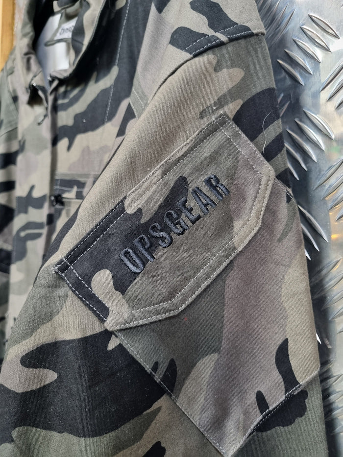 Camouflage jacket with 'OPS/GEAR' logo on a metallic surface