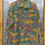 Camouflage jacket on a hanger against a metallic wall.