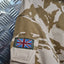 Camouflage military uniform with a British flag patch on an industrial background