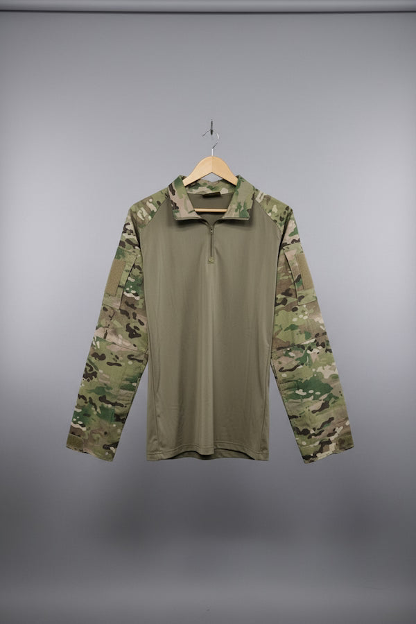 A military-style pullover shirt with a solid tan body and camouflage sleeves, hanging on a wooden hanger against a diamond plate metal door.