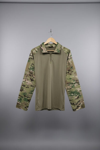 A military-style pullover shirt with a solid tan body and camouflage sleeves, hanging on a wooden hanger against a diamond plate metal door.