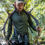 A man in outdoor gear, including a green quarter-zip fleece, cap, and harness, carrying a large pair of antlers over his shoulders in a forest setting.
