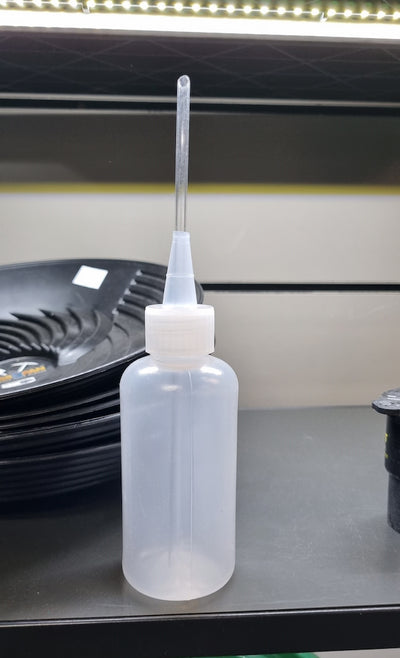A translucent plastic squeeze bottle with a long clear nozzle and a white screw cap, standing on a dark shelf.