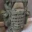 Green tactical backpack on a gray surface with a neutral background