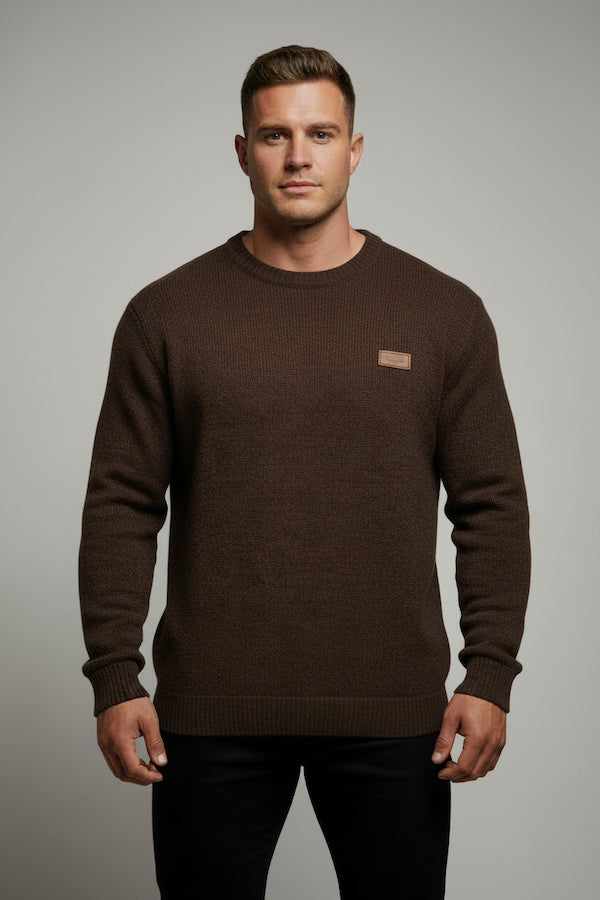 Man wearing a brown sweater with a small logo on a gray background