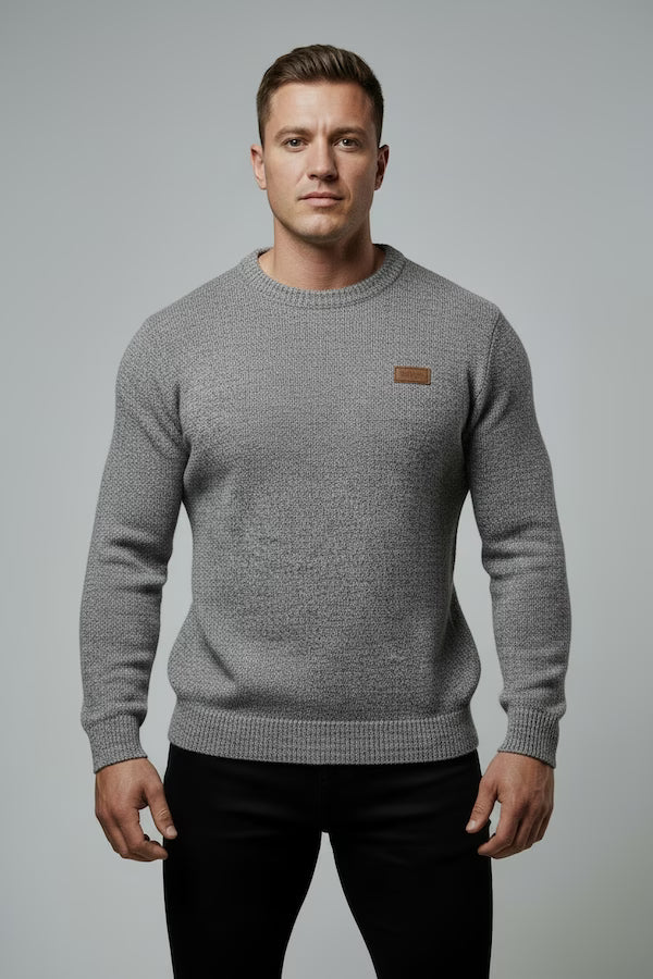 Man wearing a gray sweater with a small logo on a gray background