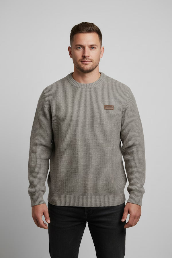 Man wearing a gray sweater with a small logo on a light gray background