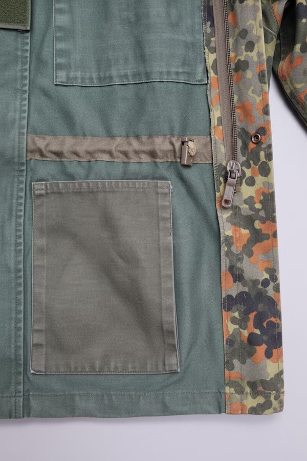 Close-up of a vintage camouflage jacket, showing a green canvas body, a brown zipper with a metal pull, and a camouflage lining.