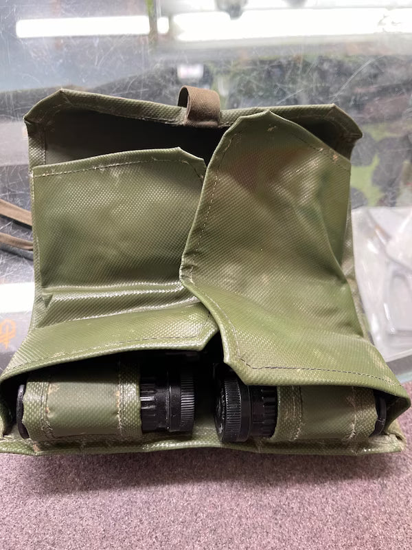 Green tactical magazine pouch with black cylindrical objects on a reflective surface
