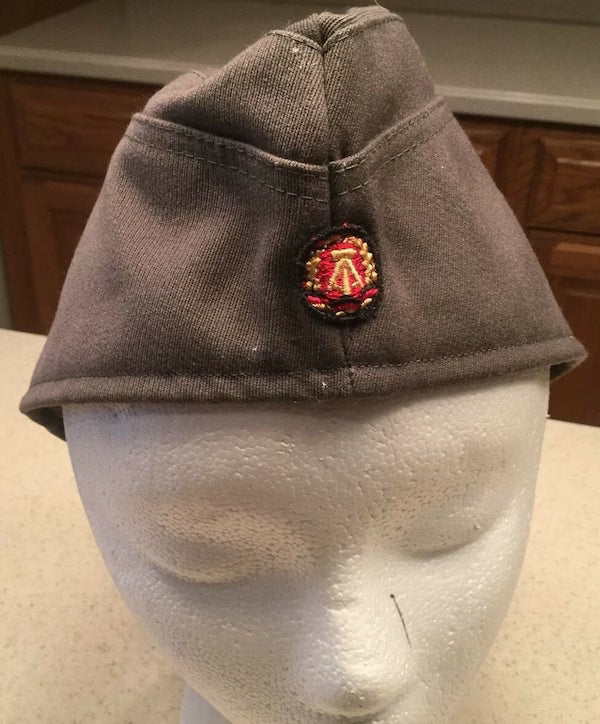 Gray cap with a embroidered badge on a mannequin head against a kitchen background