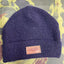 Blue knit beanie with a pink patch on a colorful abstract background
