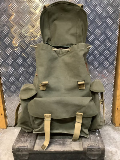 Green backpack with brown straps on a metal platform against a patterned wall.