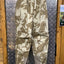 Camouflage pants hanging on a metal surface with wooden walls.