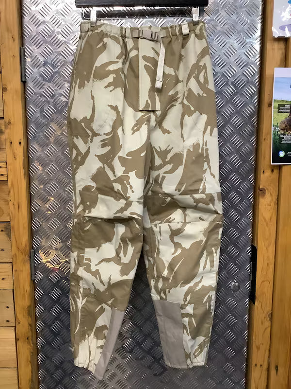 Camouflage pants hanging on a metal surface with wooden walls.