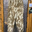 Camouflage pants hanging on a metal rod against a wooden wall.