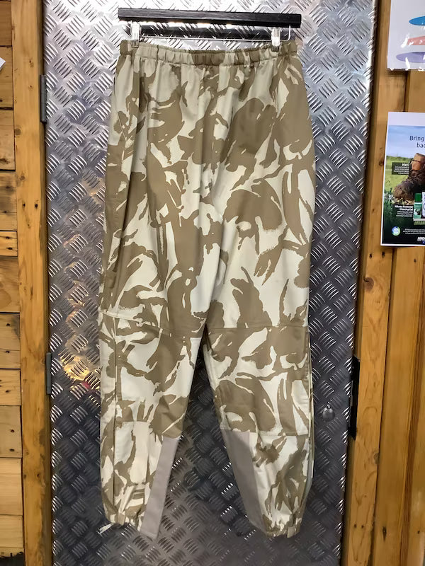Camouflage pants hanging on a metal rod against a wooden wall.
