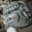 Camouflage helmet with intricate design held by a person in an indoor setting