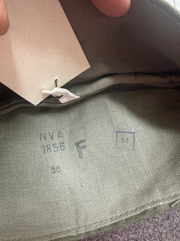 Close-up of a fabric label with 'NVA 1856 F' text on a green fabric background.