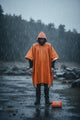 Person wearing an orange rain poncho standing in the rain with a product box on the ground.
