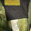 Close-up of the interior collar of a jacket showing a Kathmandu GORE-TEX Best Defence label and a white GORE-TEX tag on olive green and black fabric.