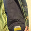 Close-up of a Katmandu jacket interior showing a dark navy inner pocket with a visible Katmandu brand patch and a yellow hook-and-loop section, next to an olive green outer fabric and zipper.