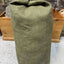Green canvas bag on a concrete floor with wooden shelves in the background