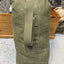 Green military-style duffel bag on a concrete floor with wooden shelves in the background.