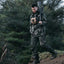 Man in camouflage walking through a forest with a rifle